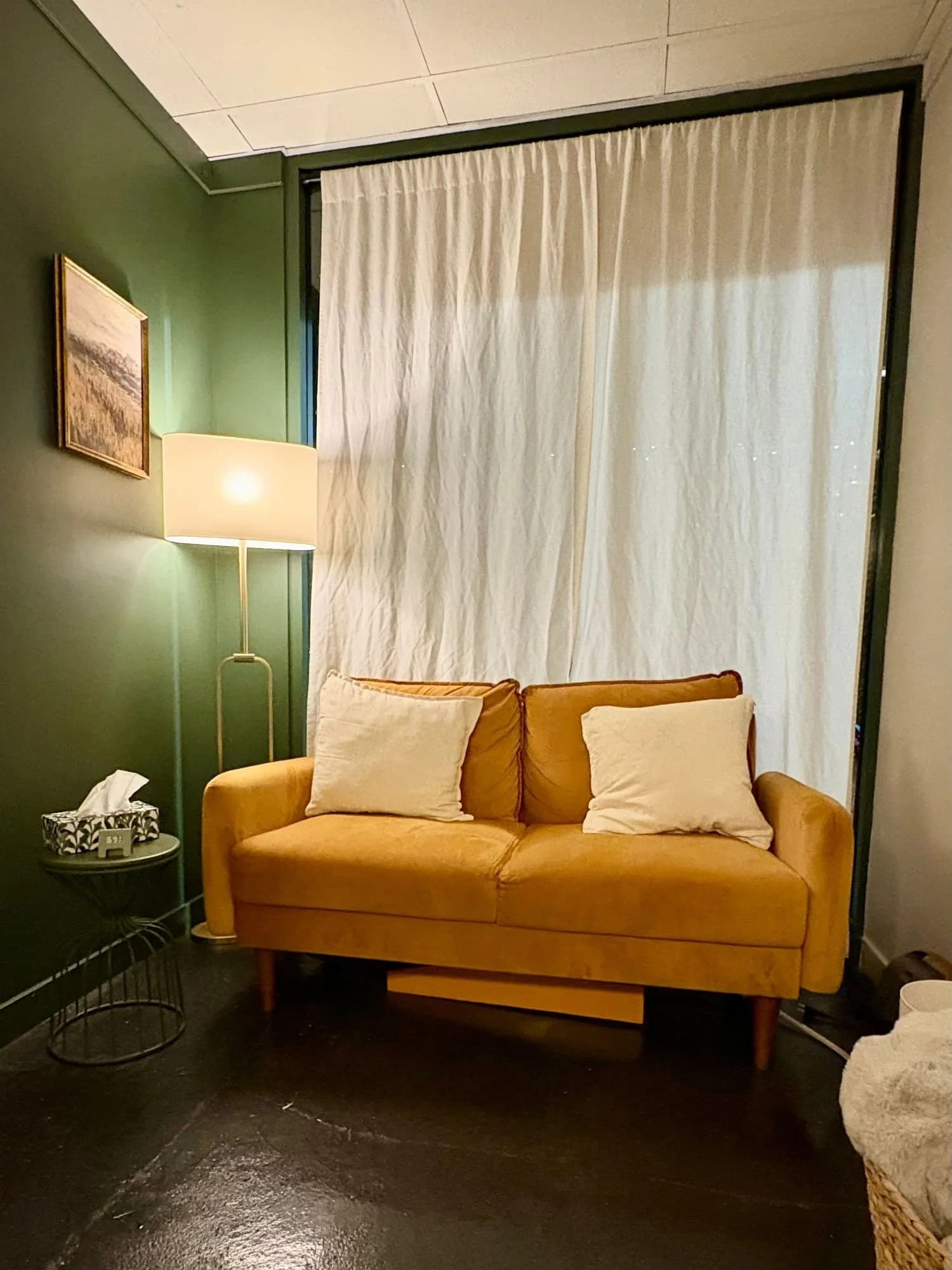 A counselling room with green walls, a lamp, and a mustard yellow sofa